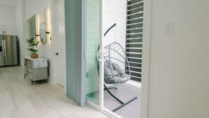 A modern kitchen with a refrigerator, a small table with a plant, and a hanging chair by a sliding glass door.