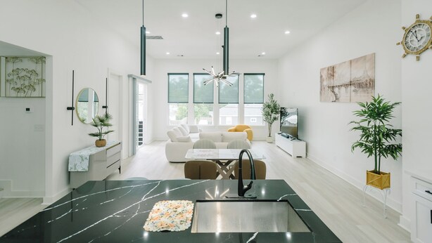 A modern kitchen with a marble countertop, a sink, and a dining area with a white table and chairs.