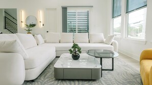 A modern living room with a white sectional sofa, a glass coffee table, and a potted bonsai tree.