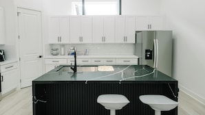 A modern kitchen with white cabinets, a black marble island, and a stainless steel refrigerator.