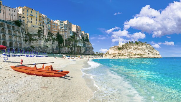 A beach with clear turquoise water, a row of beach umbrellas, and a rowboat on the sand. - Essenza Mediterranea Tropea (Tropea)