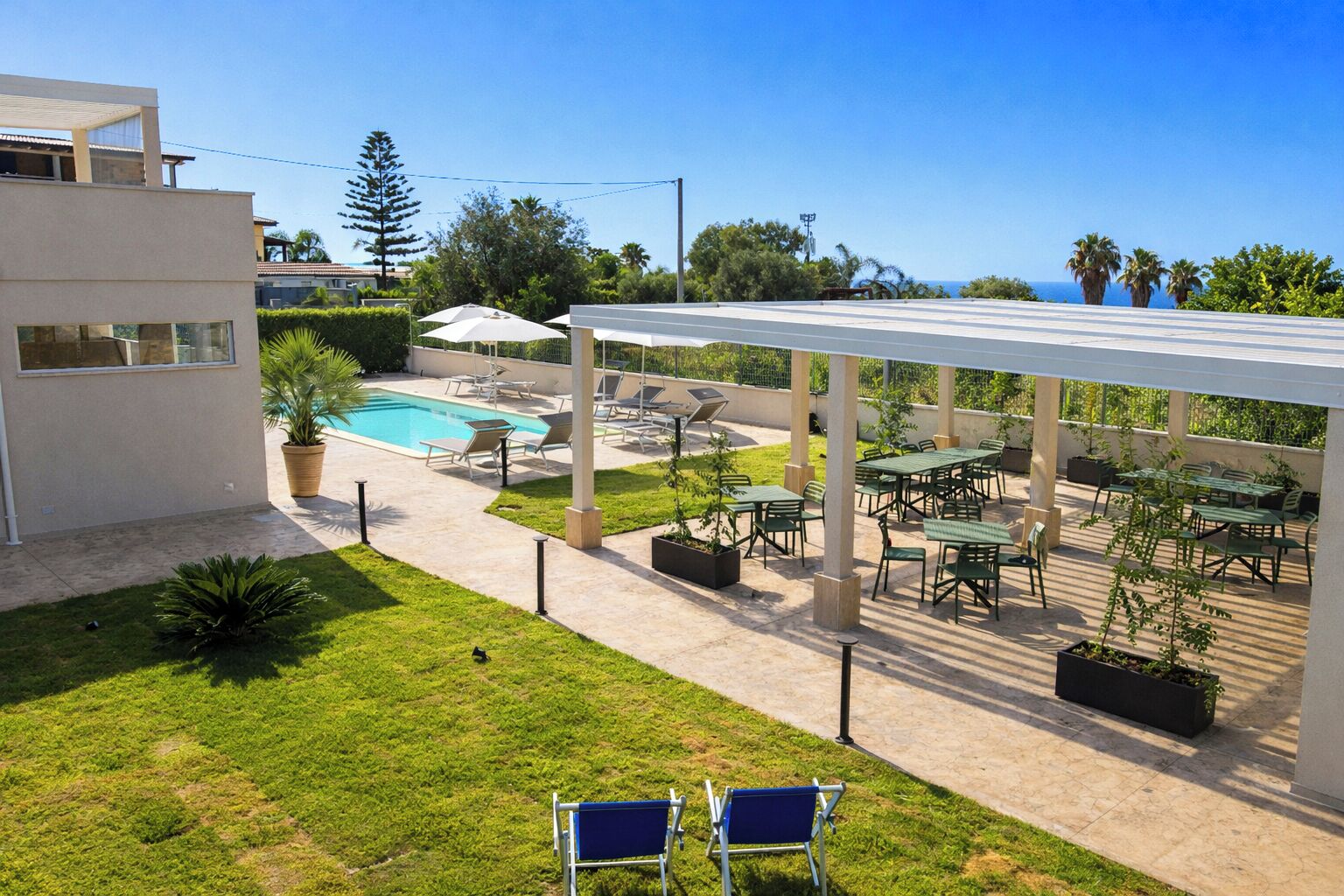 A pool area with lounge chairs and a covered patio with tables and chairs.