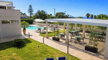 A pool area with lounge chairs and a covered patio with tables and chairs.