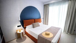 A modern hotel room with a large bed, a round blue accent wall, and a view of the outdoors through sheer curtains. - Essenza Mediterranea Tropea (Tropea)