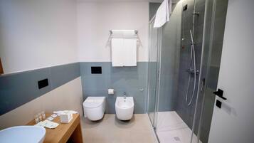 Un baño moderno con un lavamanos, dos bidés, una ducha con mampara de vidrio y un perchero para toallas.