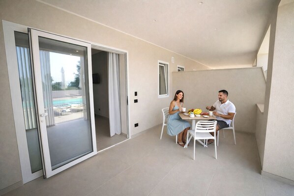 A modern apartment with a dining area, a sliding glass door leading to a balcony, and a pool in the background.