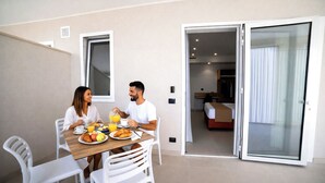 A dining area with a table set for two, a bed visible through an open door, and a small desk with a chair. - Essenza Mediterranea Tropea (Tropea)