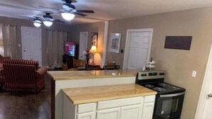 A compact kitchen with a central island, a stove, and a dining area with a red-striped couch. - ,Fern Corner: 4 bedroom / 2 Bath (Stillwater)