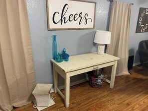 A room with a wooden floor, a white table with blue vases, a 'Cheers' sign, and a clock on the wall. - ,Newly re-finished 4 bedroom / 2 bath home (Stillwater)