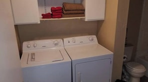 A laundry area with two stacked washers and dryers, a shelf with folded towels, and a toilet in the background. - ;Cowboy's Cottage on Fern (Stillwater)