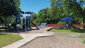 Un’area giochi con scivoli e strutture per arrampicata, circondata da alberi e un cielo sereno.