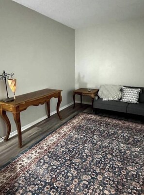 A room with a wooden bench, a small table with a lamp, a patterned rug, and a grey sofa with cushions. - West Stillwater Home (Stillwater)