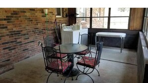 Een eethoek met een ronde tafel en vier stoelen, een wasmachine en een raam met uitzicht op een bakstenen gebouw.