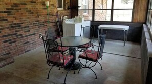 A dining area with a round table and four chairs, a washing machine, and a window with a view of a brick building.