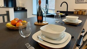 A modern kitchen with a central island, a fruit basket, wine bottle, and glasses. - Retreat In The Hills - The Old Post Office (Malvern)