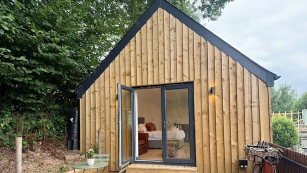 A wooden cabin with a sliding glass door leading to a bedroom with a bed and a sofa. - Retreat In The Hills - The Old Post Office (Malvern)
