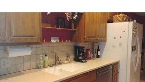 A kitchen with wooden cabinets, a white countertop, a sink, and a refrigerator. - Cowboys' Home with a Hot Tub (Stillwater)