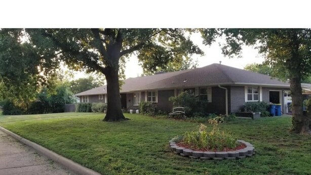 A single-story house with a front yard, a tree, and a small garden bed. - Cowboys' Home with a Hot Tub (Stillwater)
