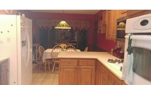 A kitchen with wooden cabinets, a dining table with chairs, a refrigerator, and an oven. - Cowboys' Home with a Hot Tub (Stillwater)