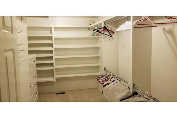 A walk-in closet with multiple shelves and hanging space, a mirror, and a coat rack.