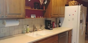Een keuken met houten kastjes, een wit aanrecht, een spoelbak en een koelkast.