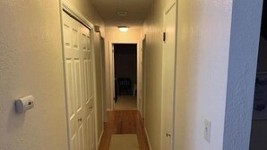 A narrow hallway with white walls and wooden flooring, leading to a dark room at the end. - Crestwood Bungalow (Stillwater)