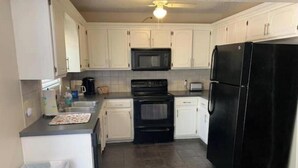 A compact kitchen with white cabinets, a black refrigerator, a microwave, and a stove. - Crestwood Bungalow (Stillwater)