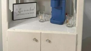 Een witte kast met een rode magnetron op het bovenste plank, een blauwe waterdispenser en een lijst met een citaat op het middelste plank.