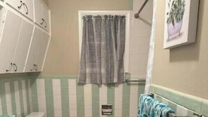 Een badkamer met een betegelde muur in strepen, een toilet, een wastafel met een lichtblauwe tas op het aanrecht en een handdoekhouder met een handdoek.