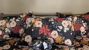 Una habitació amb un sofà de disseny floral, un rètol fixat a la paret amb la paraula "gather" i una corona sobre una finestra.