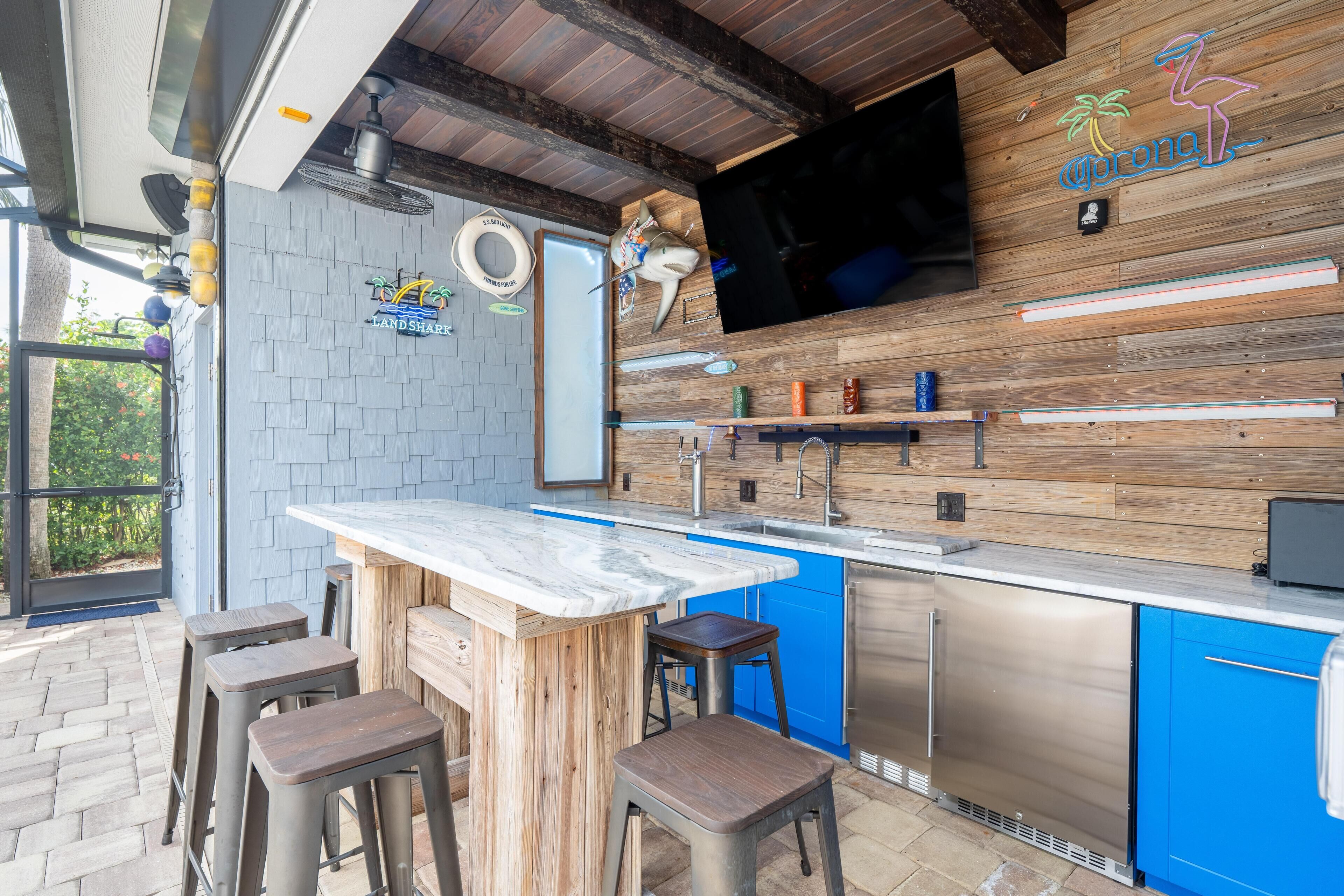Una cocina al aire libre con encimera de mármol, gabinetes azules y un refrigerador de acero inoxidable.