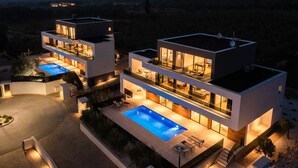 Ein modernes, mehrgeschossiges Haus mit Swimmingpool, Außenbereich zum Sitzen und Blick auf die umliegende Landschaft.