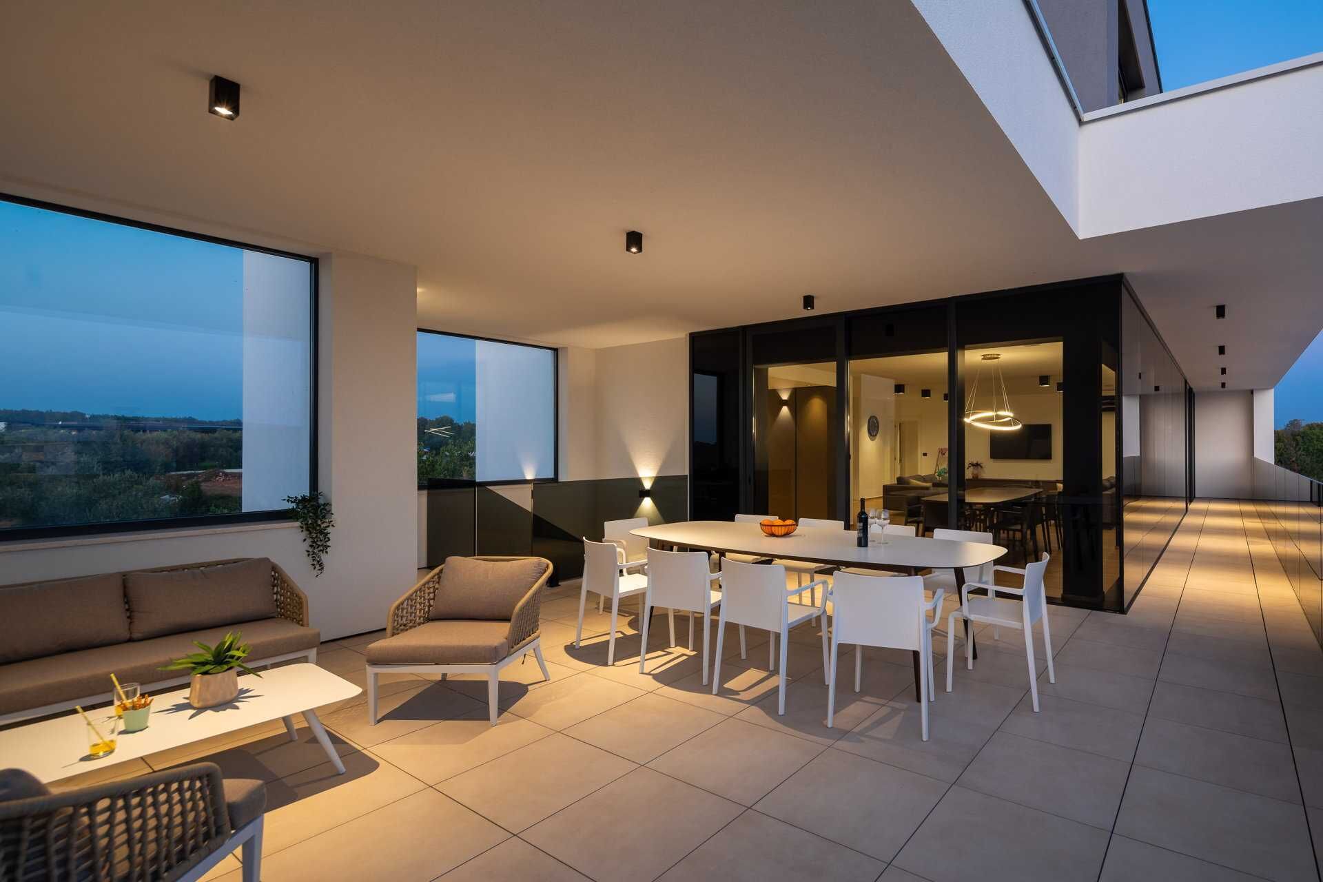 A modern outdoor dining area with a white table and chairs, a sofa, and a view of the landscape.