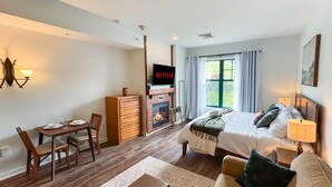 A hotel room with a bed, a TV, a fireplace, a dining area, and a window with curtains. - Heated Pool Hot Tubs Sauna Gym Mtn Front Appalachian @ Mtn Creek #428 (Vernon)