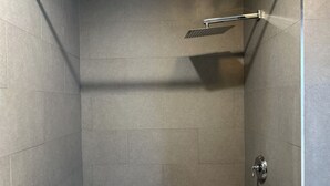 En dusch med ett duschmunstycke som kan hållas i handen, en väggmonterad blandare och en flaska schampo på golvet.