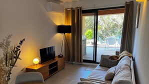 Un salon moderne avec un téléviseur à écran plat posé sur un meuble en bois, un canapé, une table à manger et une grande fenêtre avec des rideaux.