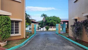 A residential street with two-story houses, a clear sky, and a central road leading to a gate. - 3-bedroom townhome in lovely Couva with AC, fitness room (Couva)