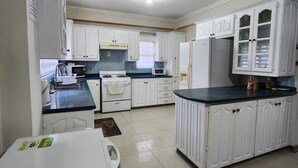 A kitchen with white cabinets, a black countertop, and a refrigerator. - 3-bedroom townhome in lovely Couva with AC, fitness room (Couva)