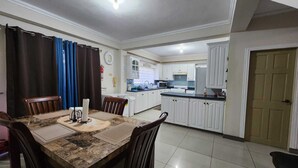 A dining area with a marble table, chairs, and a kitchen in the background. - 3-bedroom townhome in lovely Couva with AC, fitness room (Couva)