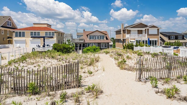 Une propriété située en bord de mer, avec un chemin de sable menant à une maison dotée d’un balcon.