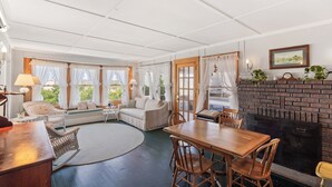 Un salon chaleureux avec une cheminée, un coin repas et un espace détente avec un canapé et des fauteuils.