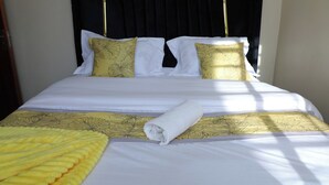 Un letto rifatto con biancheria da letto bianco e giallo, un asciugamano arrotolato e una coperta gialla.