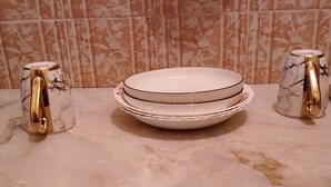 Un tavolo con piano in marmo, con piatti bianchi impilati e due caraffe di vetro decorative con manici dorati.