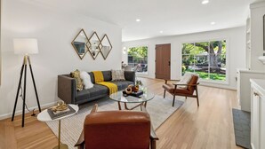 Una sala de estar moderna con un sofá, una mesa de centro y sillas. Hay una lámpara, un espejo y una ventana con vistas al exterior.
