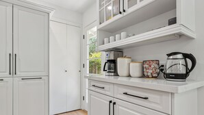 Una cocina moderna con armarios blancos, una cafetera, un hervidor y una jarra de café sobre la encimera.