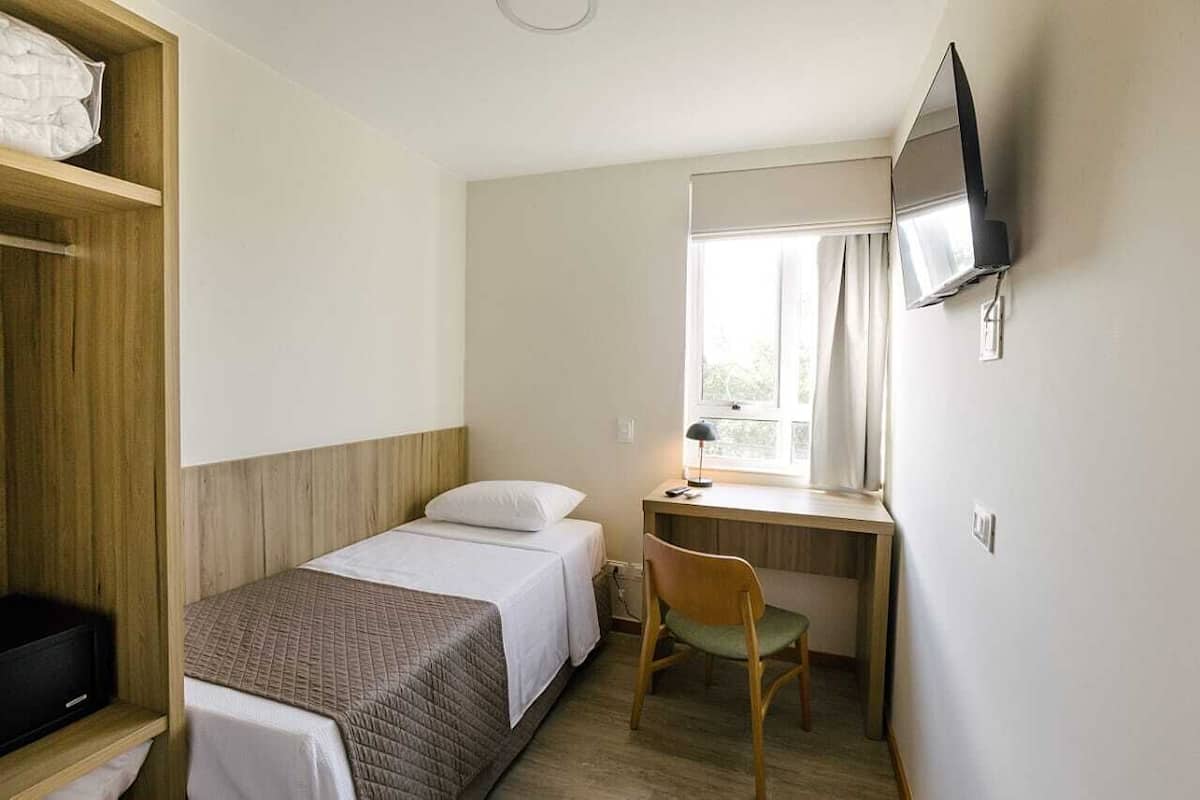 A small, compact room with a bed, a desk, a chair, and a television mounted on the wall.