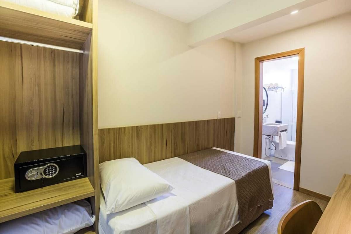 A hotel room with a bed, a wooden wardrobe, and a small desk.