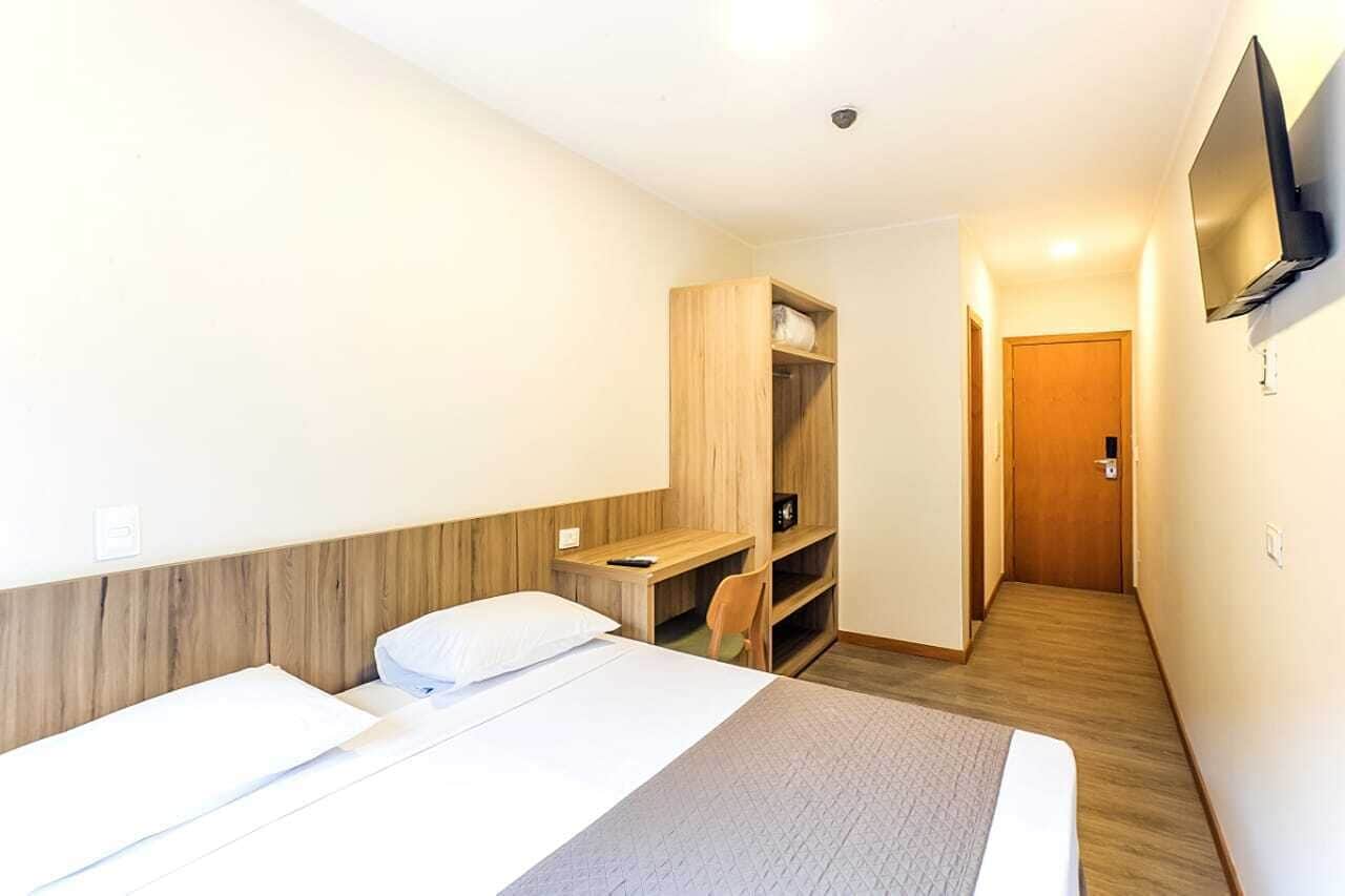 A hotel room with two beds, a wooden wardrobe, a desk, a chair, and a TV mounted on the wall.