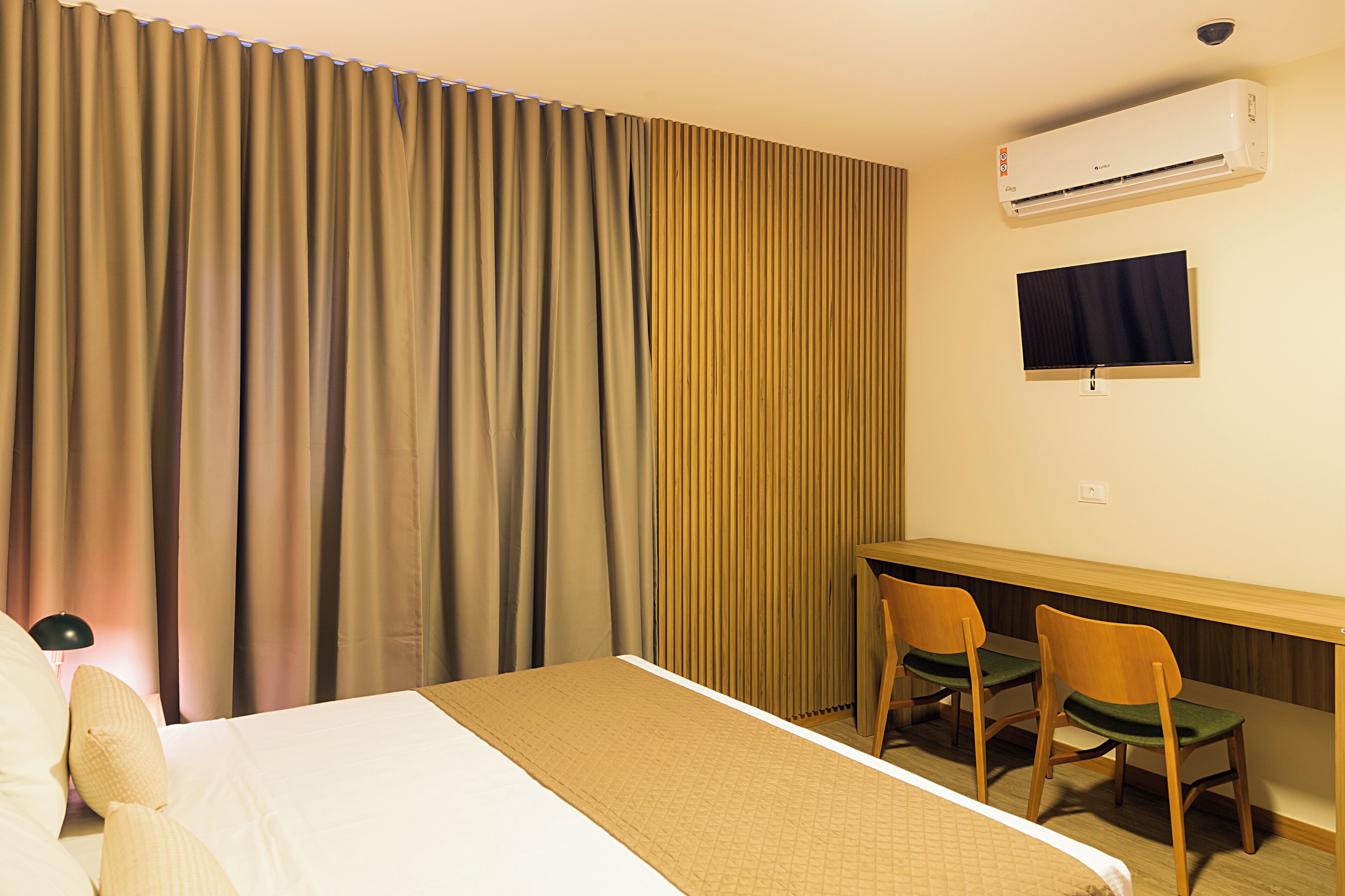 A hotel room with a bed, a desk, two chairs, an air conditioner, and a television.