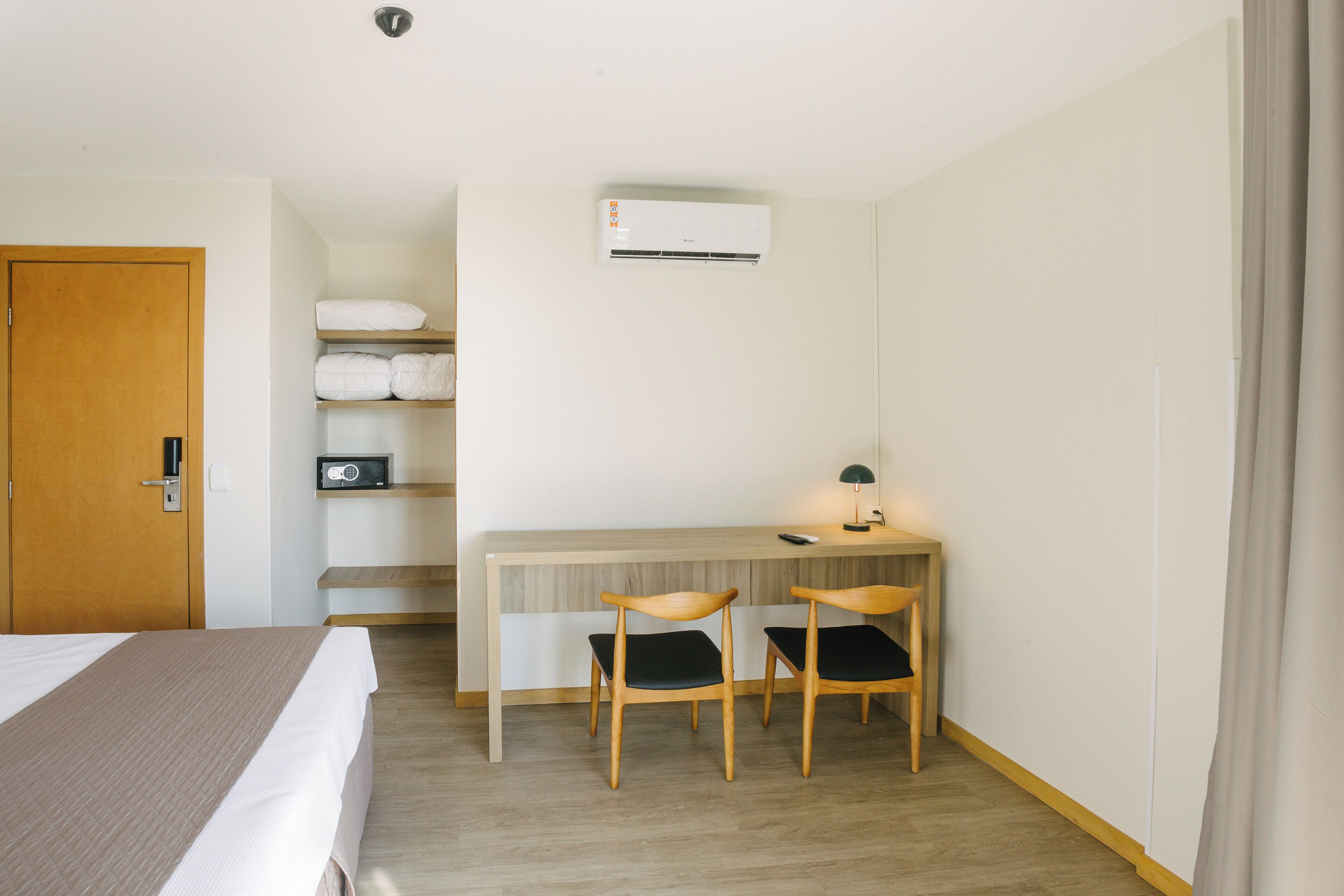 Une chambre d’hôtel comprenant un lit, un bureau avec deux chaises, un appareil de climatisation et une porte.